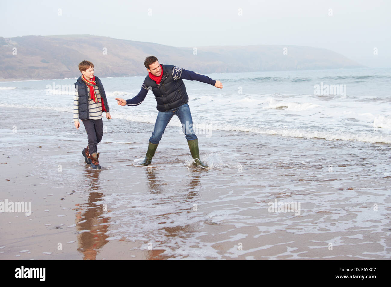 Father And Son Walking On Winter Beach And Throwing Stones Stock Photo