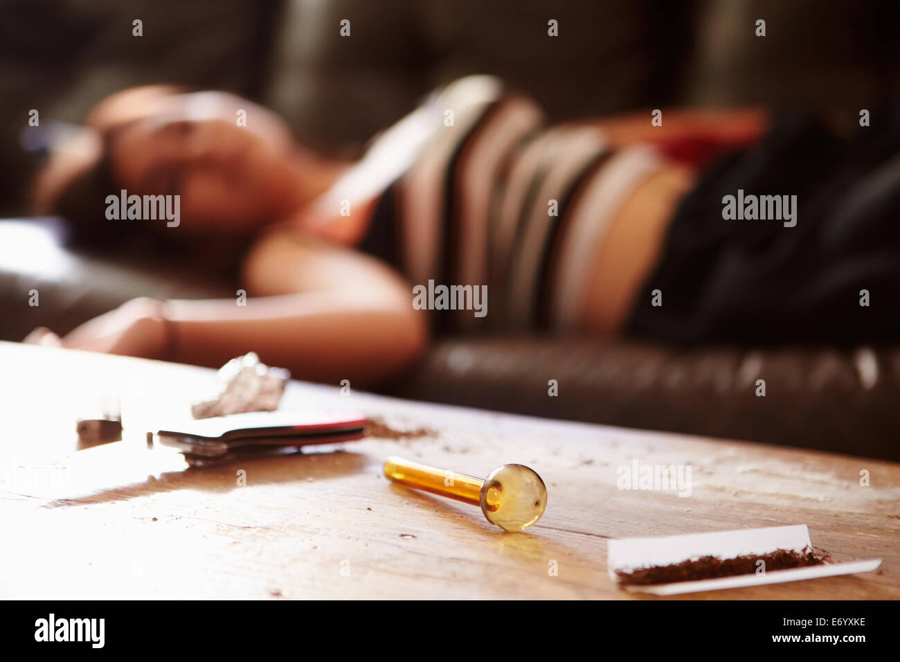 Woman Slumped On Sofa With Drug Paraphernalia In Foreground Stock Photo