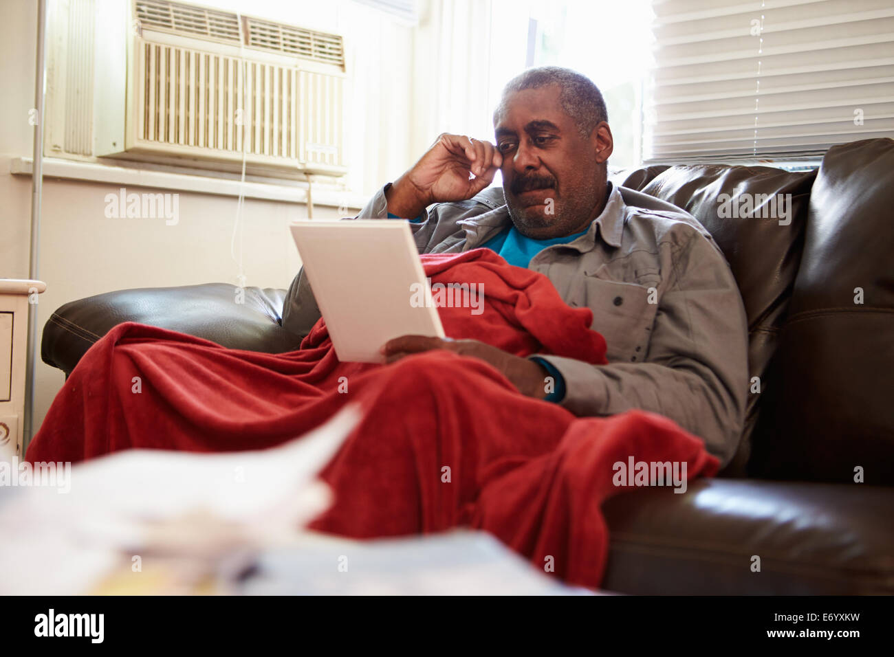 Senior Man Keeping Warm Under Blanket With Photograph Stock Photo