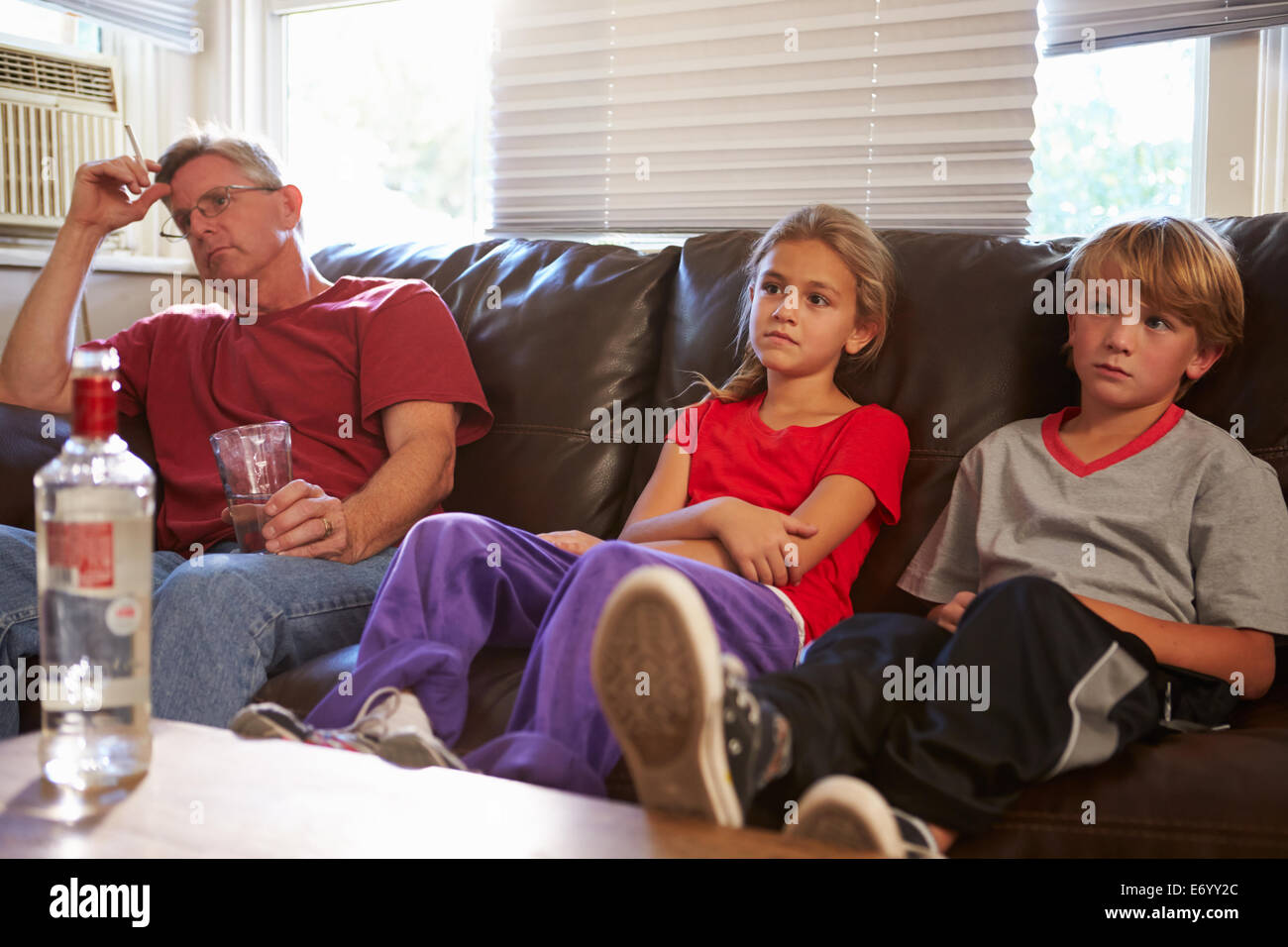 Father Sits On Sofa With Children Smoking And Drinking Stock Photo