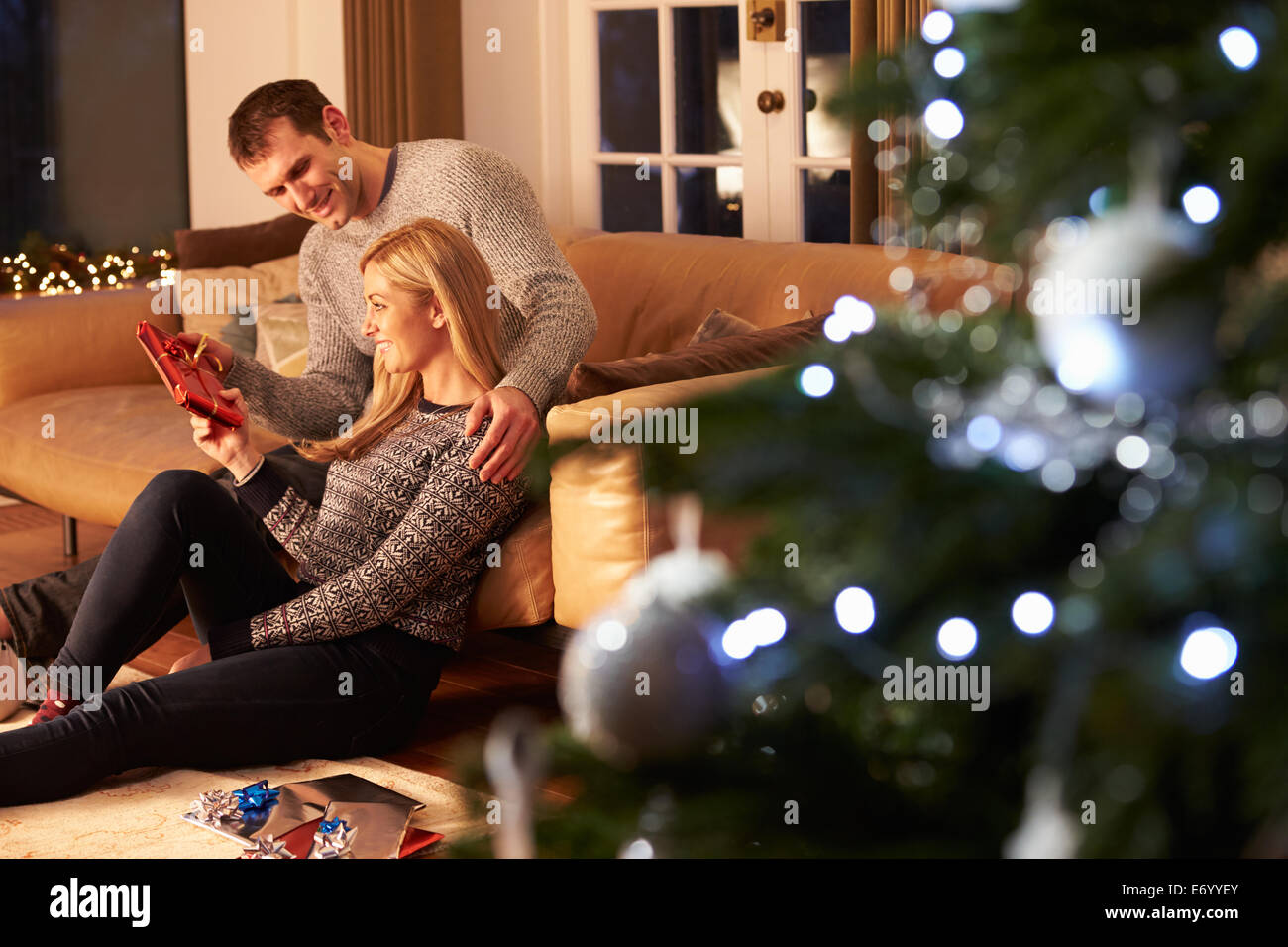 Couple Exchanging Gifts By Christmas Tree Stock Photo