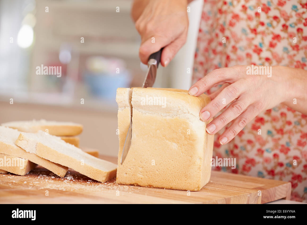 Close Up Of Woman Slicing Loaf Of Bread In Kitchen Stock Photo