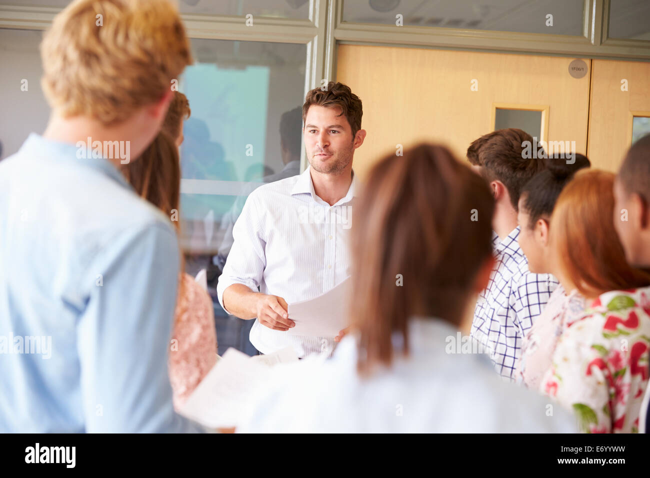 Teacher With College Students Standing By Desks In Classroom Stock Photo
