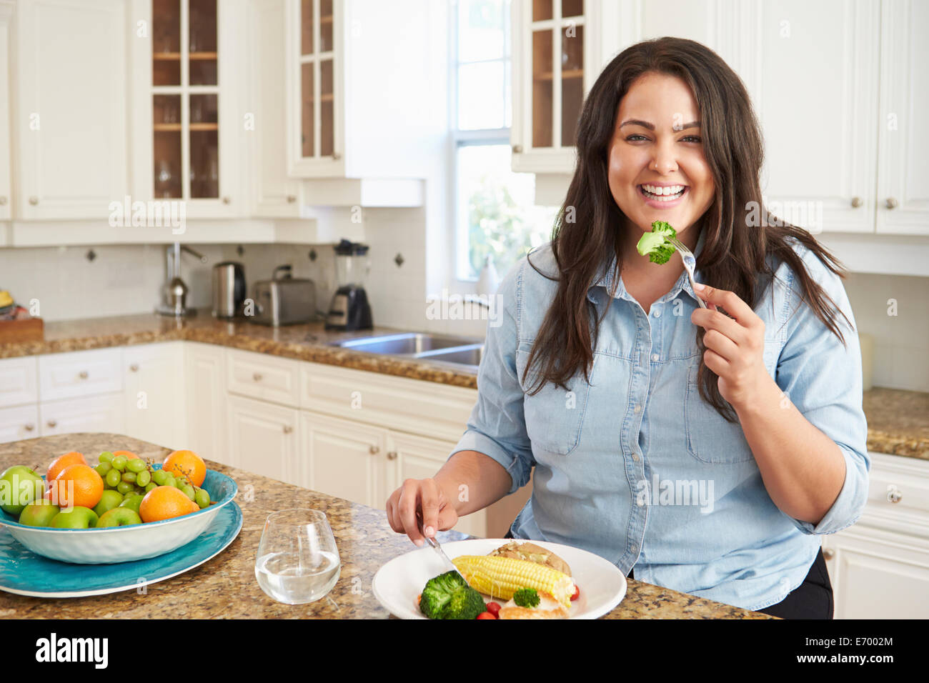 Overweight Woman Eating Healthy Meal In Kitchen Stock Photo