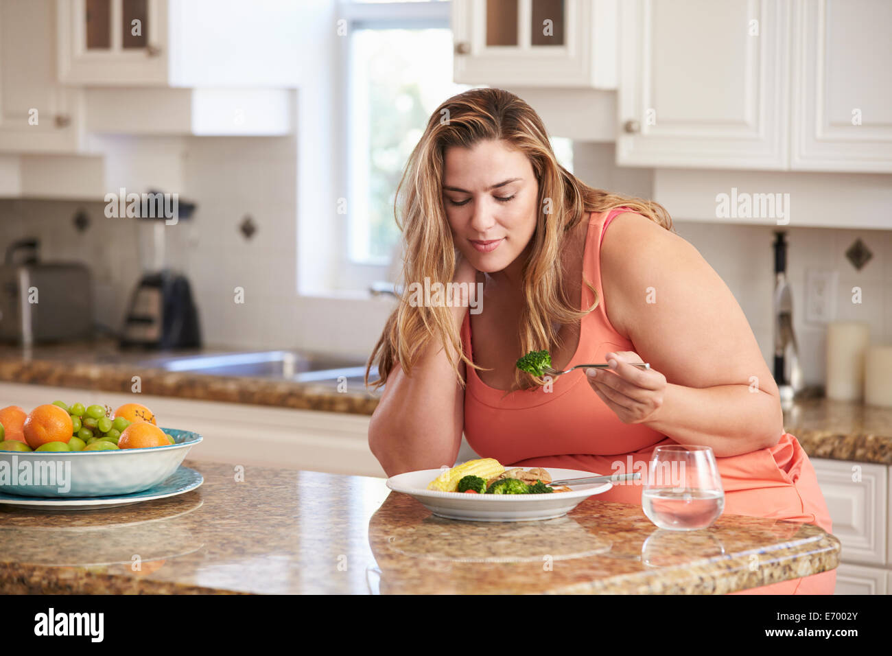 Overweight Woman Eating Healthy Meal In Kitchen Stock Photo