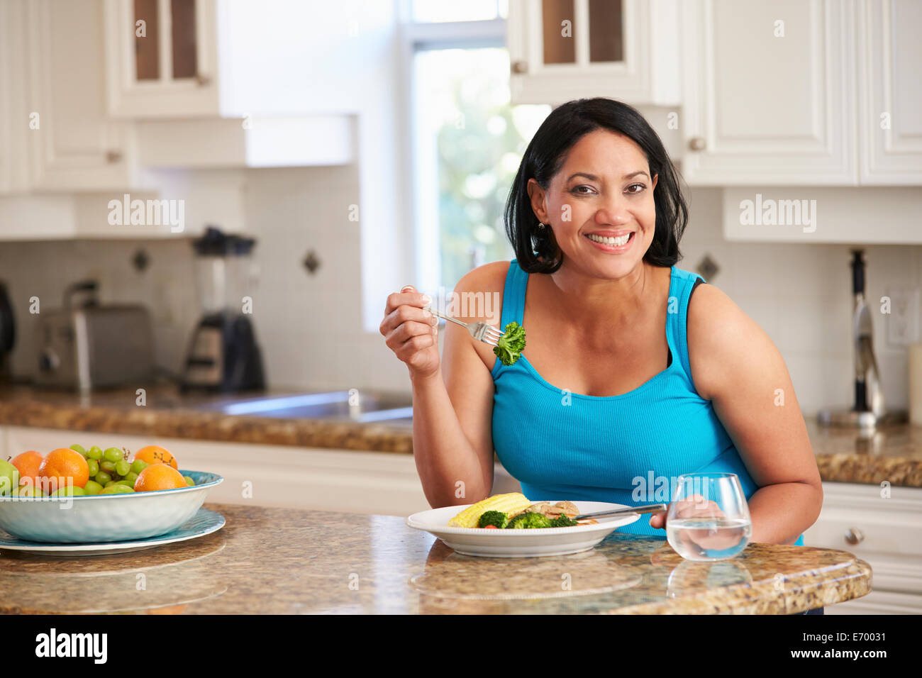 Overweight Woman Eating Healthy Meal in Kitchen Stock Photo