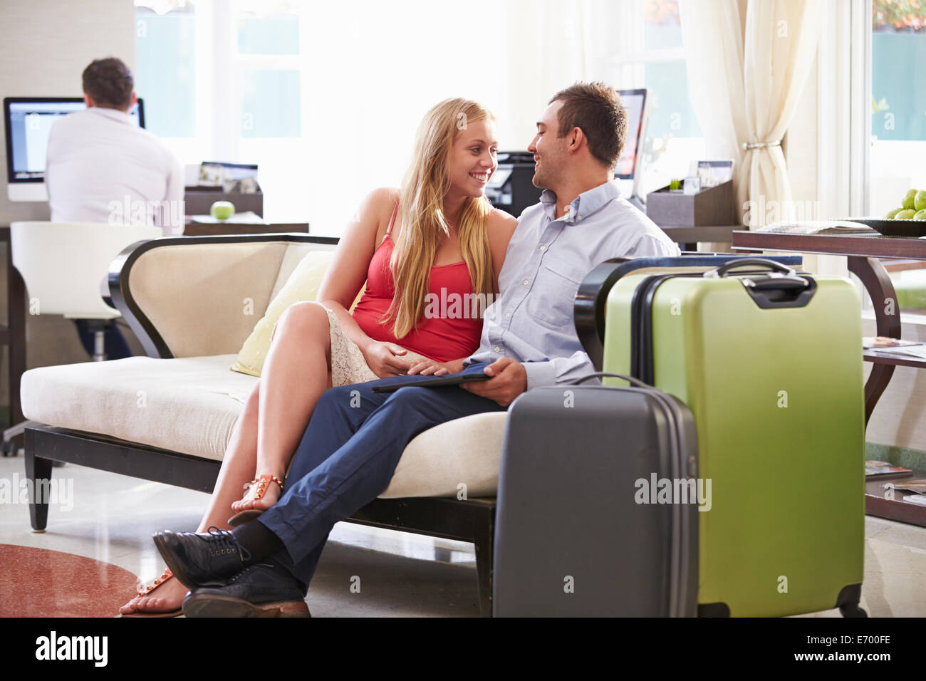 Couple Sitting In Hotel Lobby With Luggage Stock Photo