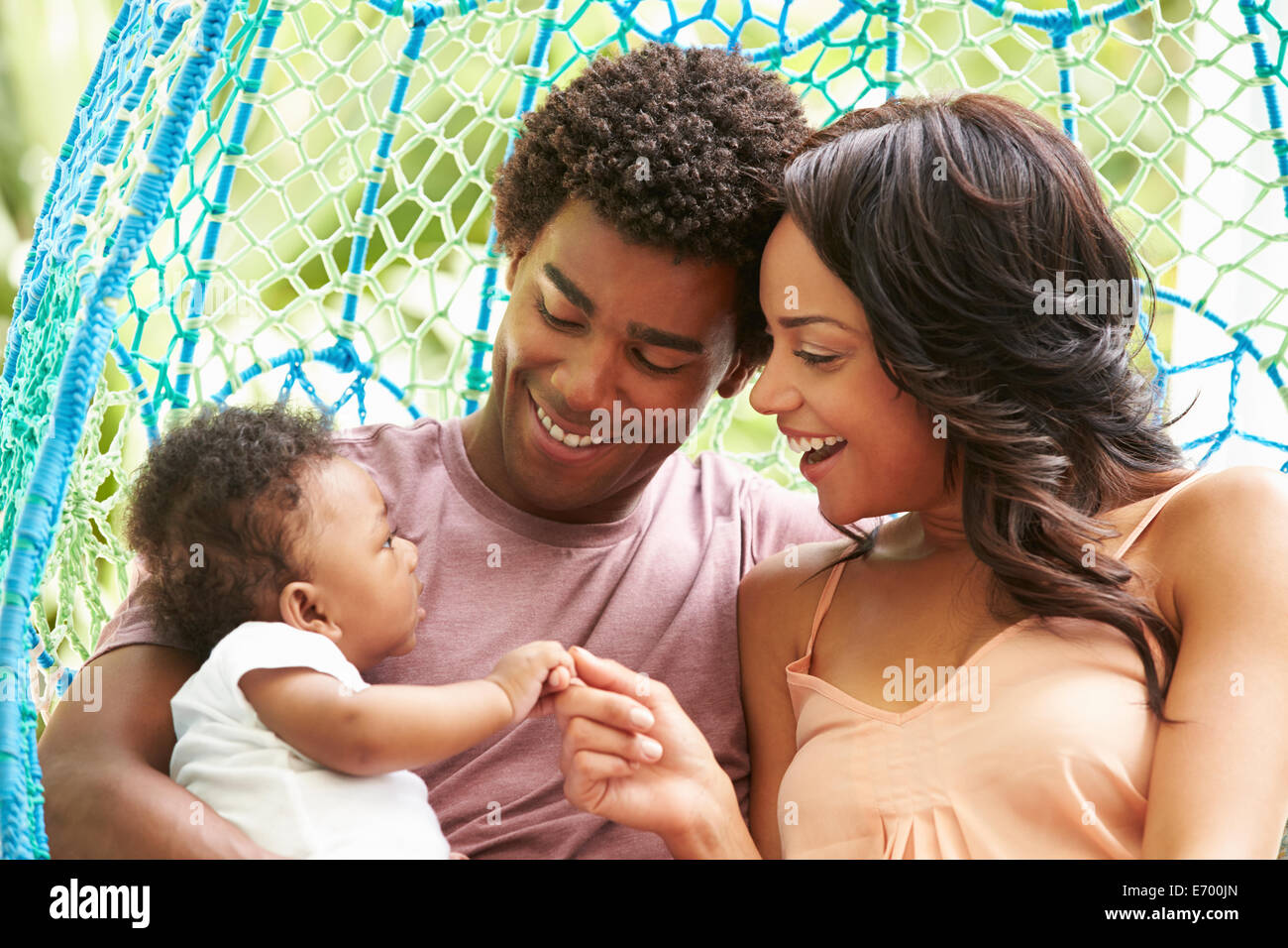 Family With Baby Relaxing On Outdoor Garden Swing Seat Stock Photo