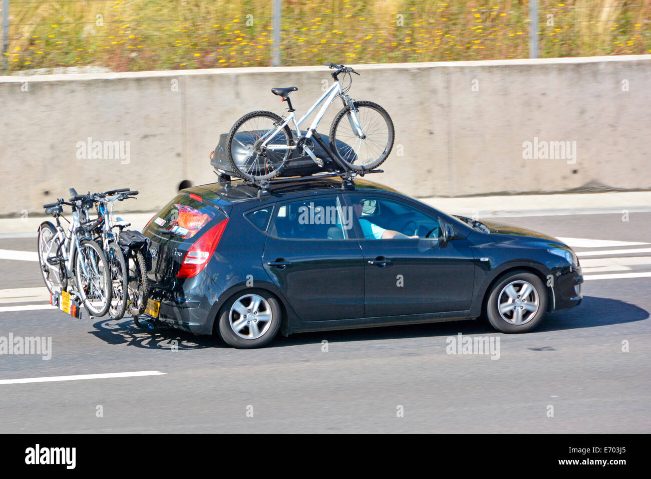Car driving along motorway with roof rack & top box fitted with bike also with rear mounted cycle rack (obscured numberplates) Stock Photo