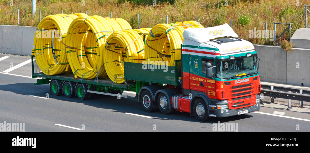 Side and front view haulage contractor Scania lorry truck with articulated trailer loaded with large coils of flexible yellow gas pipes on UK motorway Stock Photo