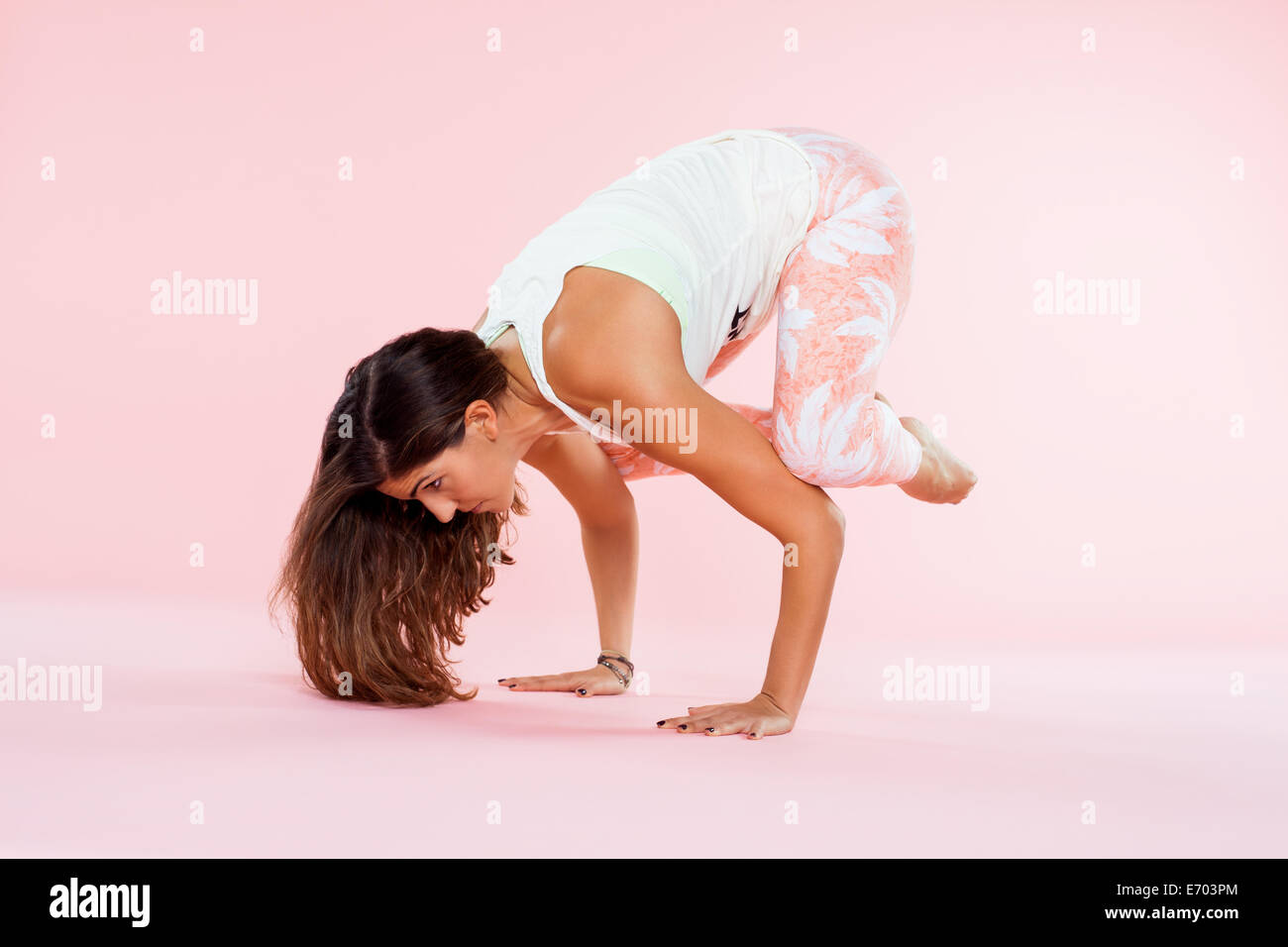 Studio shot of young woman in yoga position balancing with hands on floor and knees on elbows Stock Photo