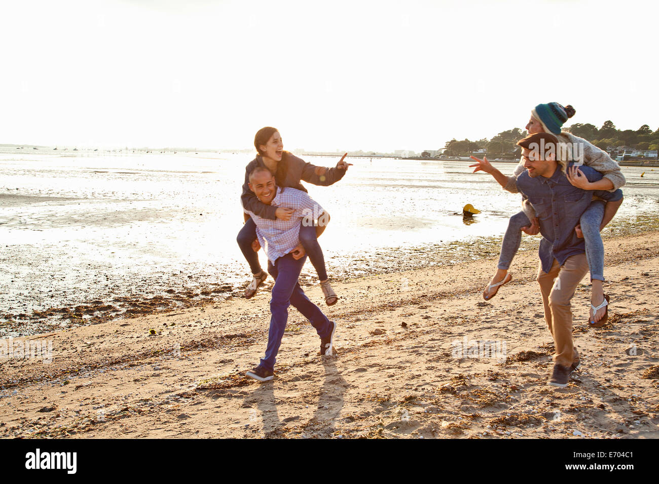 Men giving piggyback ride to women on beach Stock Photo