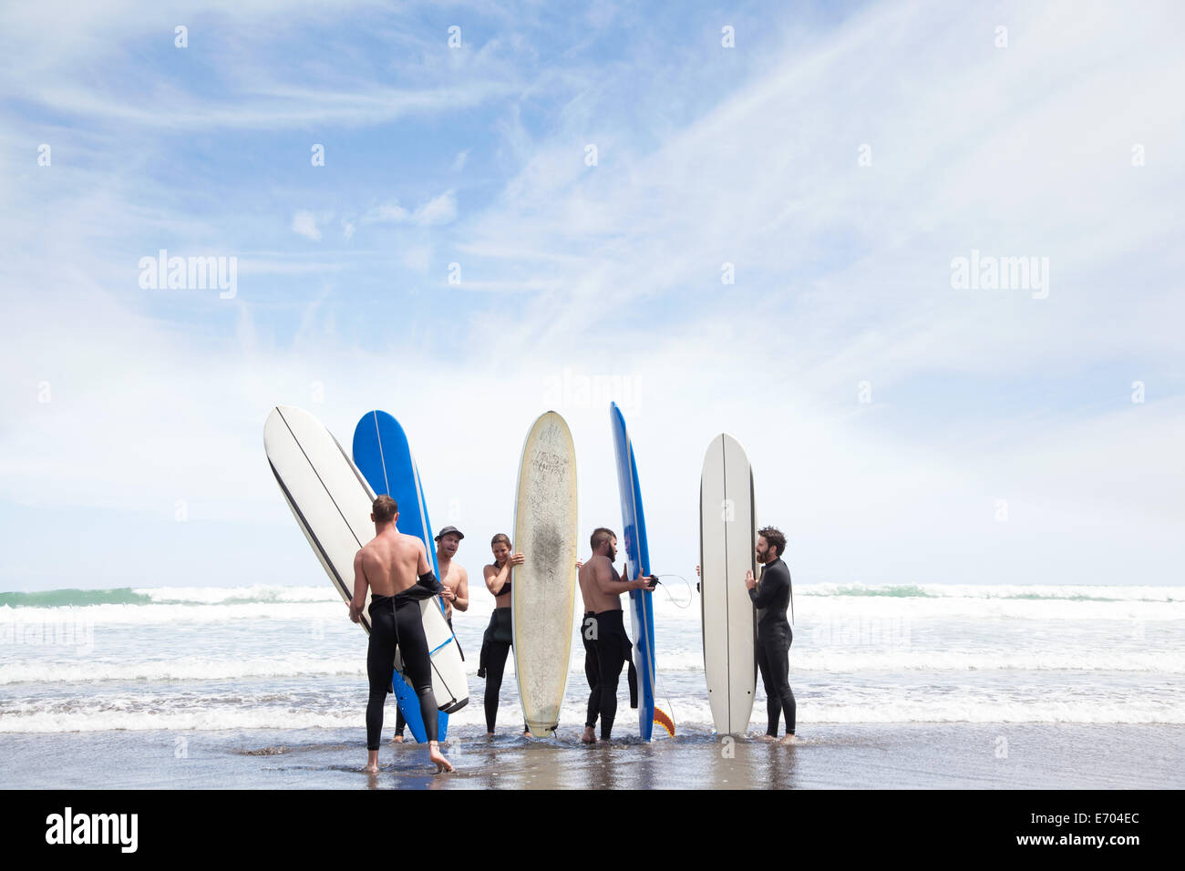 Group of male and female surfer friends standing on beach with surf boards Stock Photo