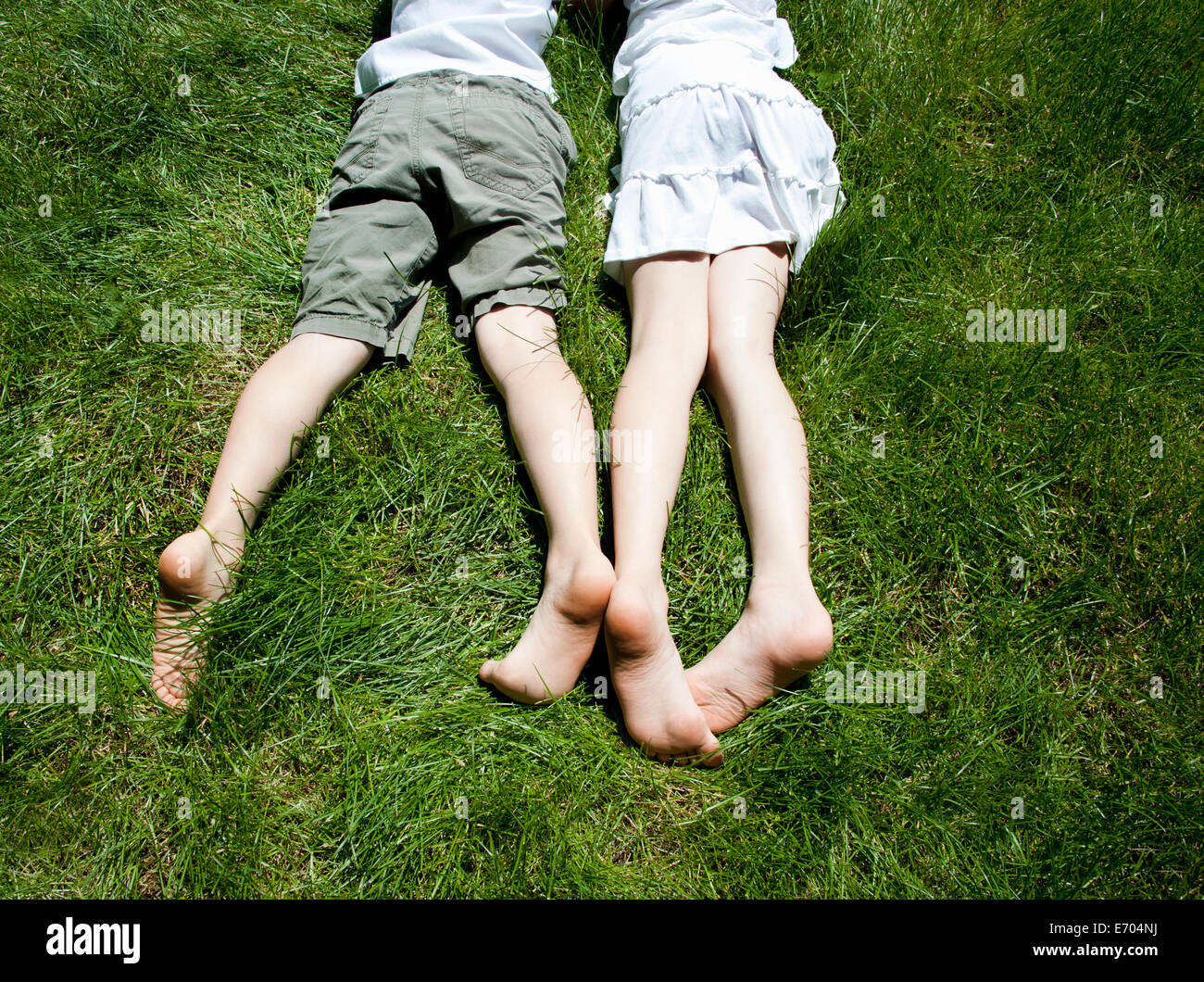 Overhead view of brother and sisters legs as they lay on grass Stock