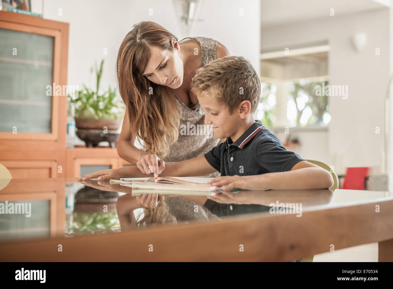Mother and son looking down at homework at dining room table Stock Photo