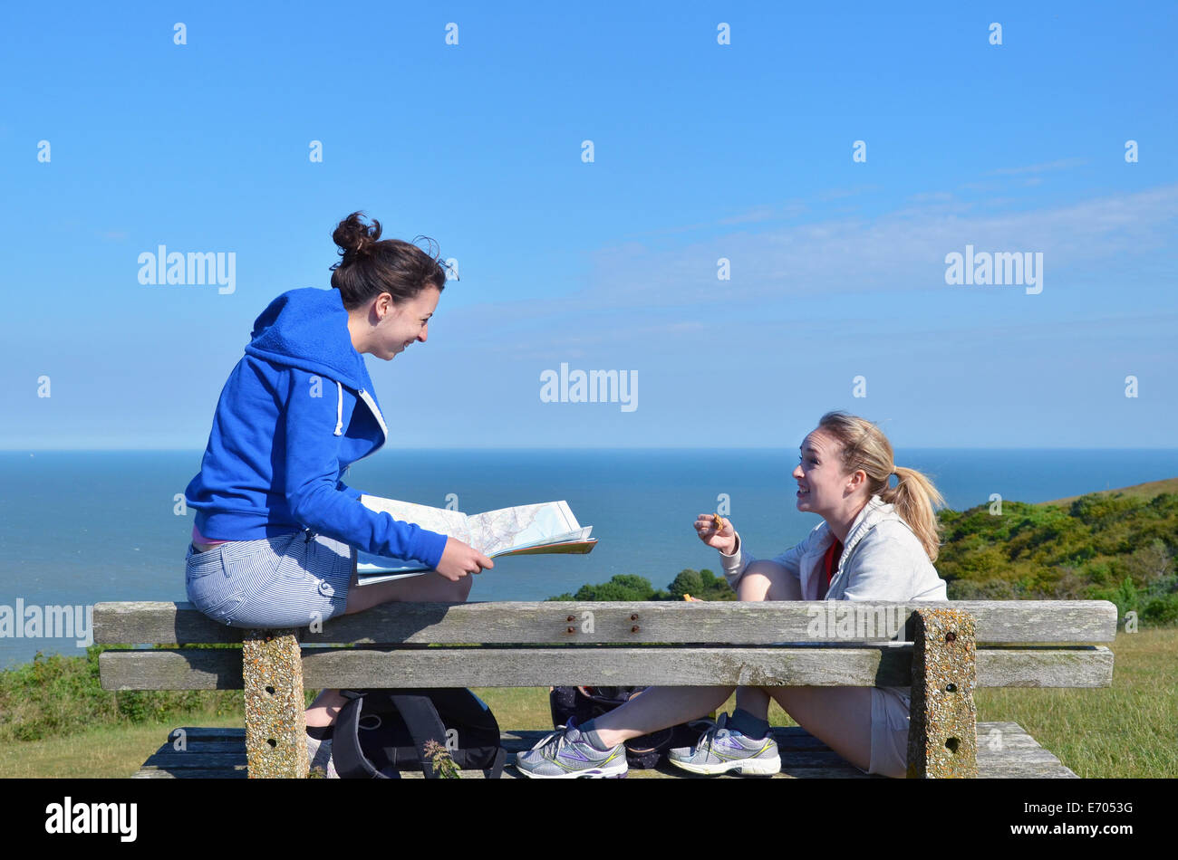 Two young women sitting on bench with map Stock Photo