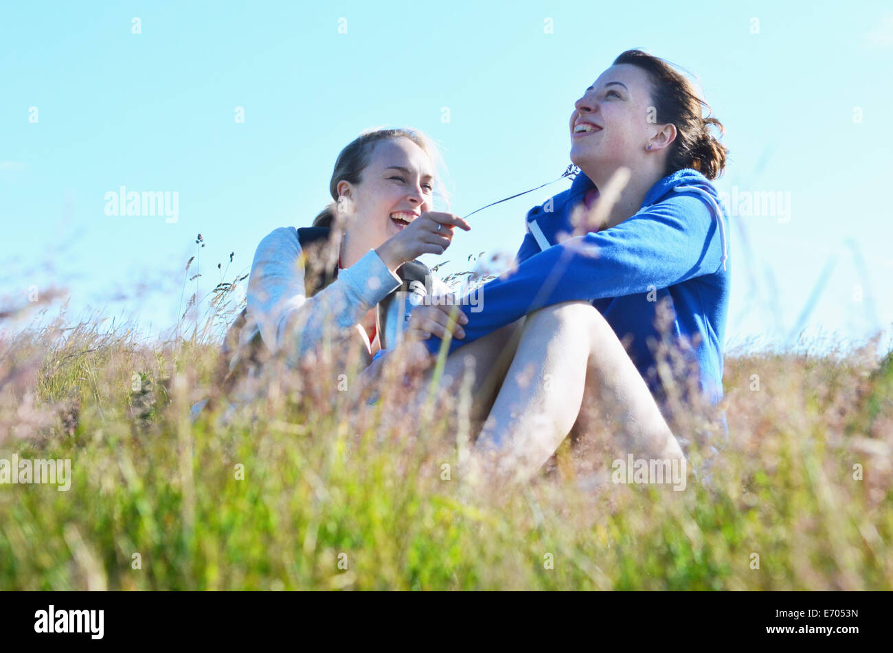 Two young women sitting field, one tickling the other Stock Photo