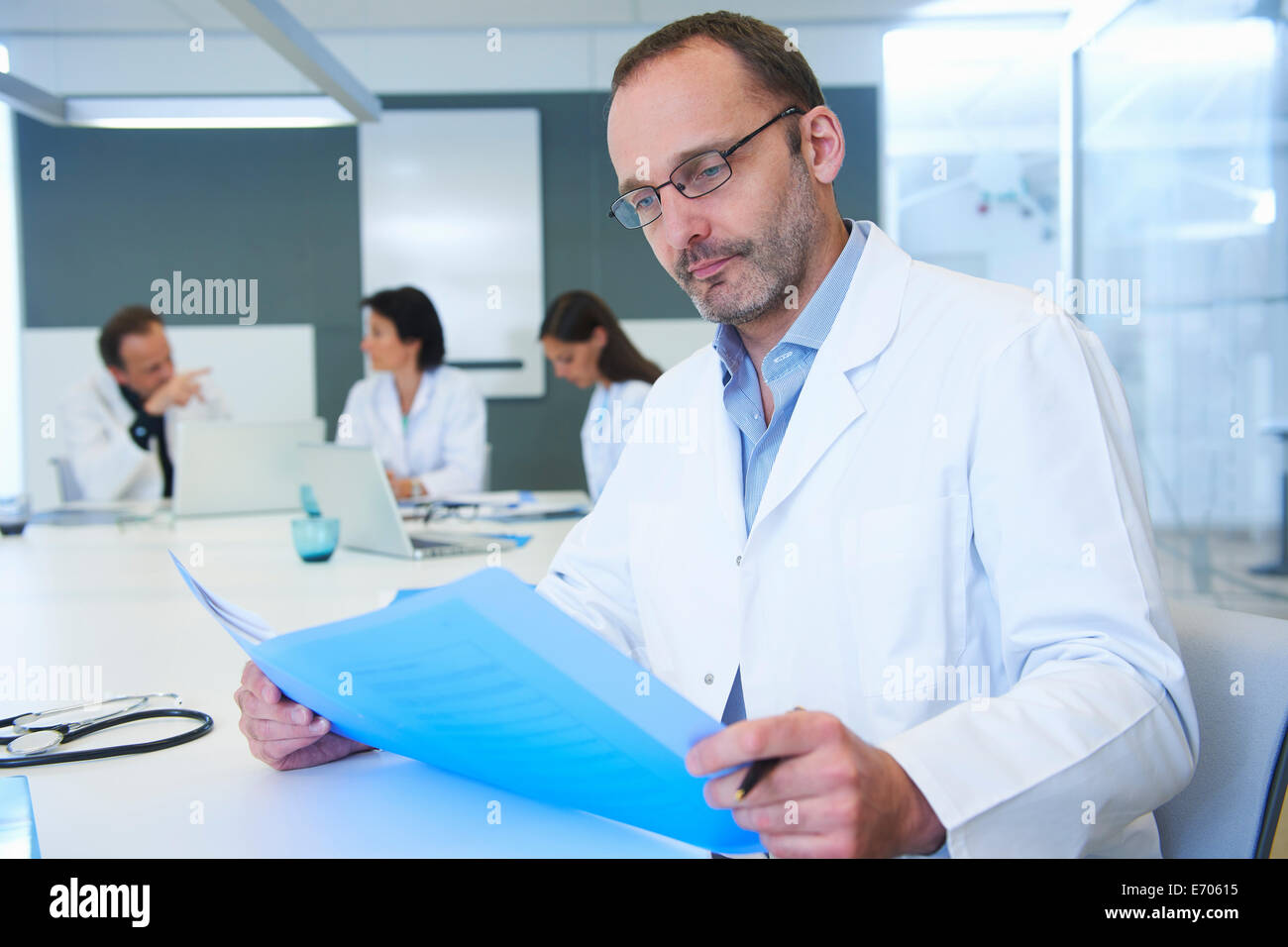 Male doctor looking at records, colleagues having discussion behind Stock Photo