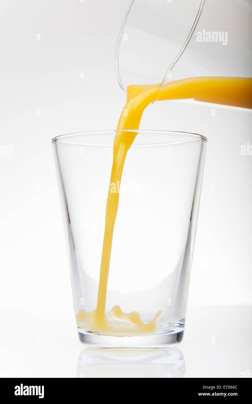 Fresh orange juice pouring from jug into drinking glass Stock Photo