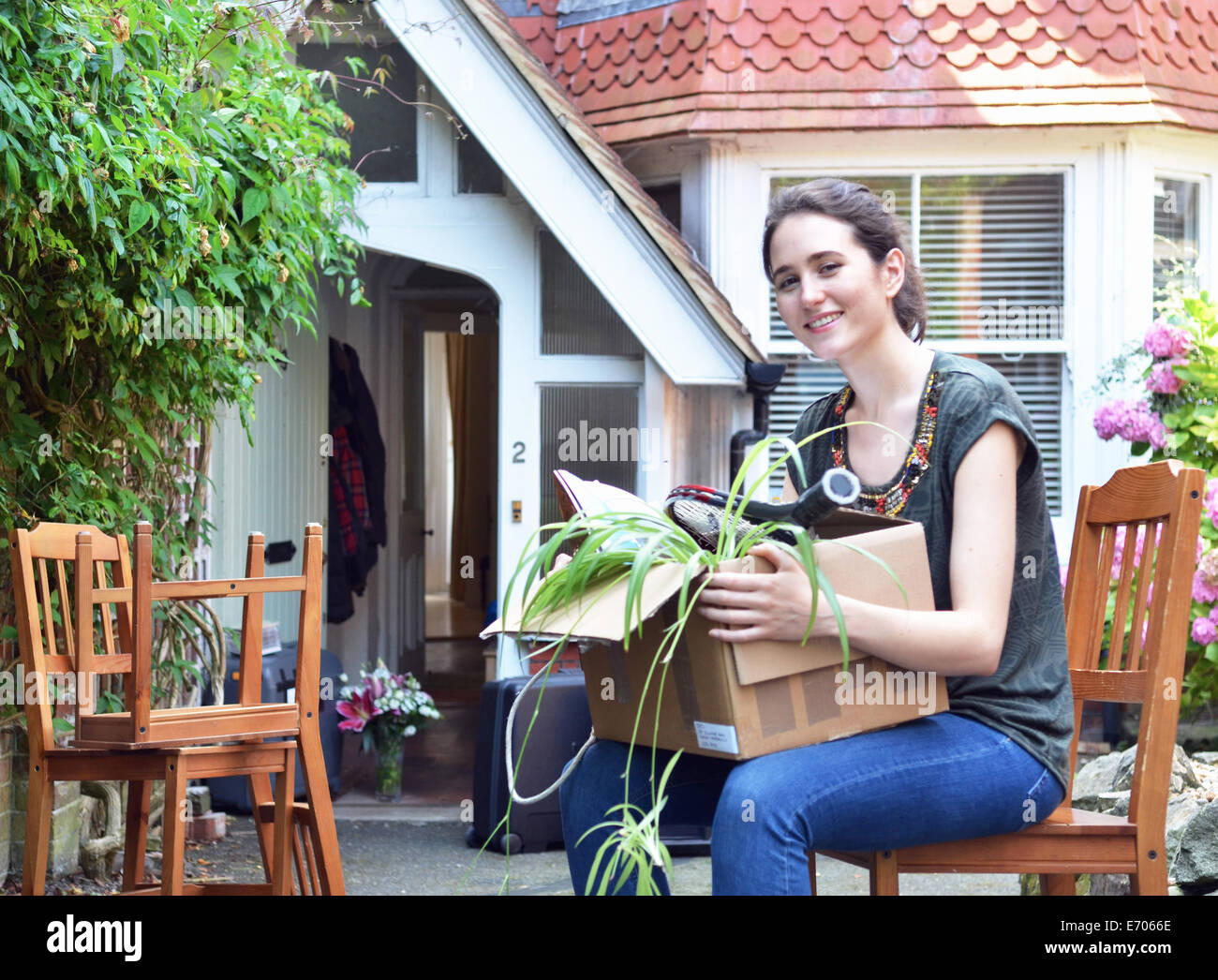 Young woman sitting outside new house with cardboard box Stock Photo