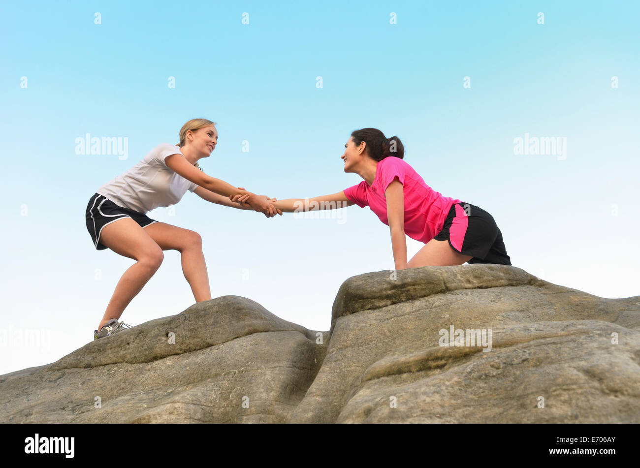 Young female runner helping friend to top of rock formation Stock Photo