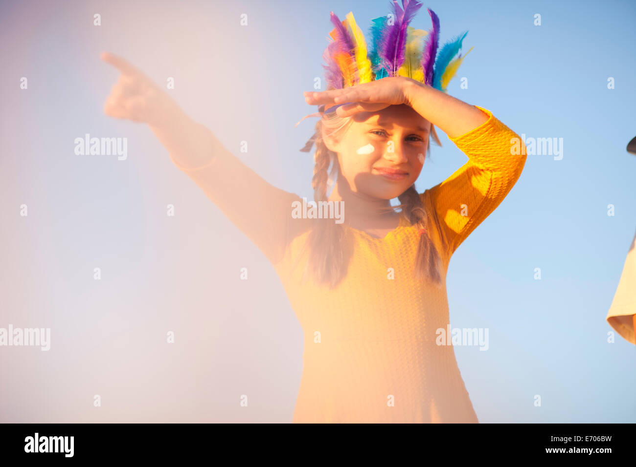 Girl dressed as native american in feather headdress with hand shading eyes and pointing Stock Photo