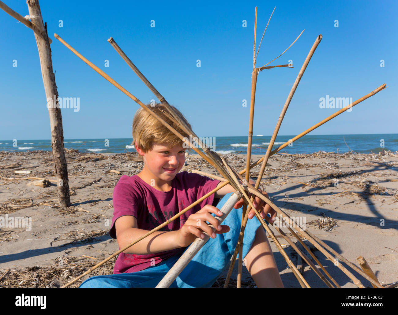 Boy constructing a circular structure from driftwood, Caleri Beach, Veneto, Italy Stock Photo