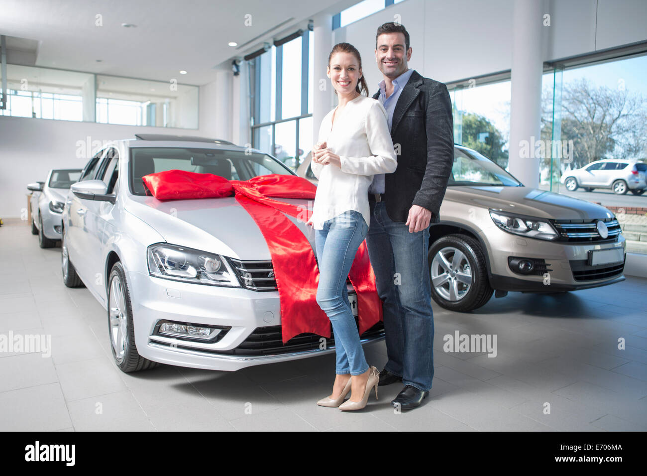 Portrait of mid adult couple and new car with red bow in car dealership
