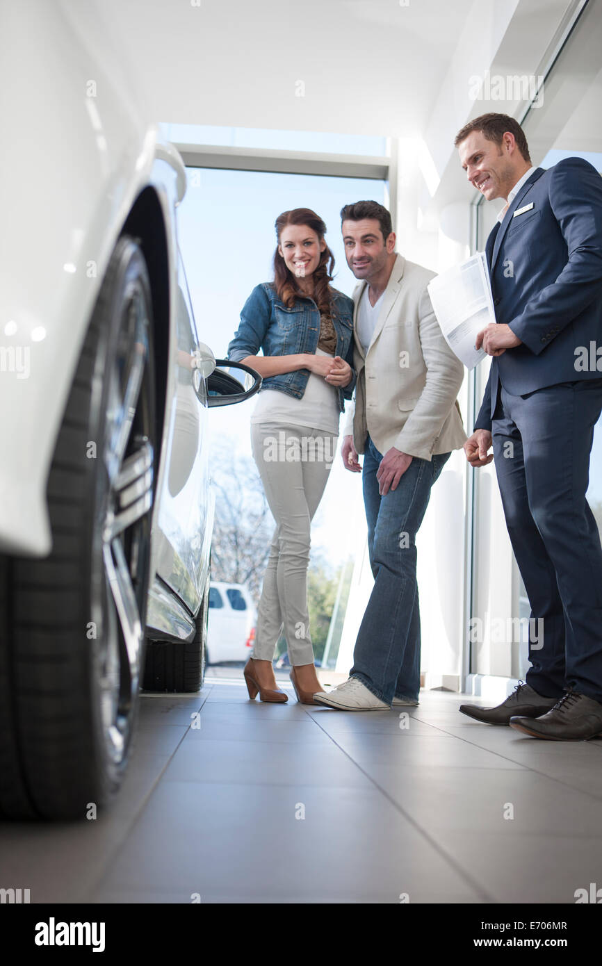 Mid adult couple and salesman looking at car in car dealership Stock Photo