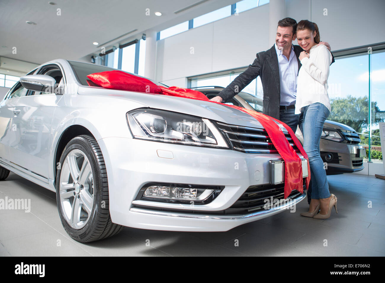 Man looking at new car with red bow with girlfriend in car dealership