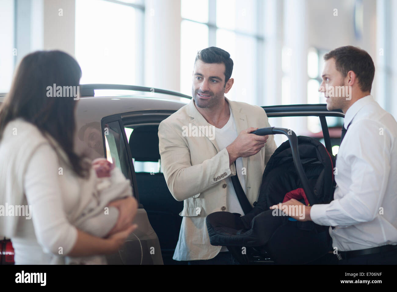 Mid adult couple with baby girl chatting about baby seat in car dealership Stock Photo