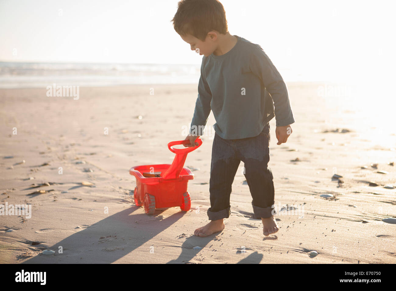 Boy pulling toy truck filled with sand along beach Stock Photo