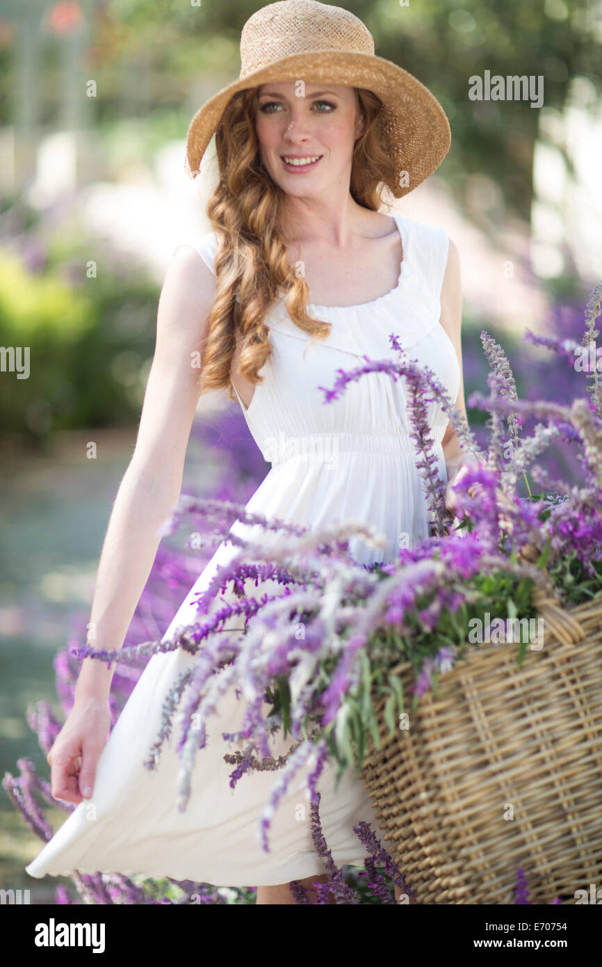 Portrait of beautiful young woman in garden with basket of purple ...