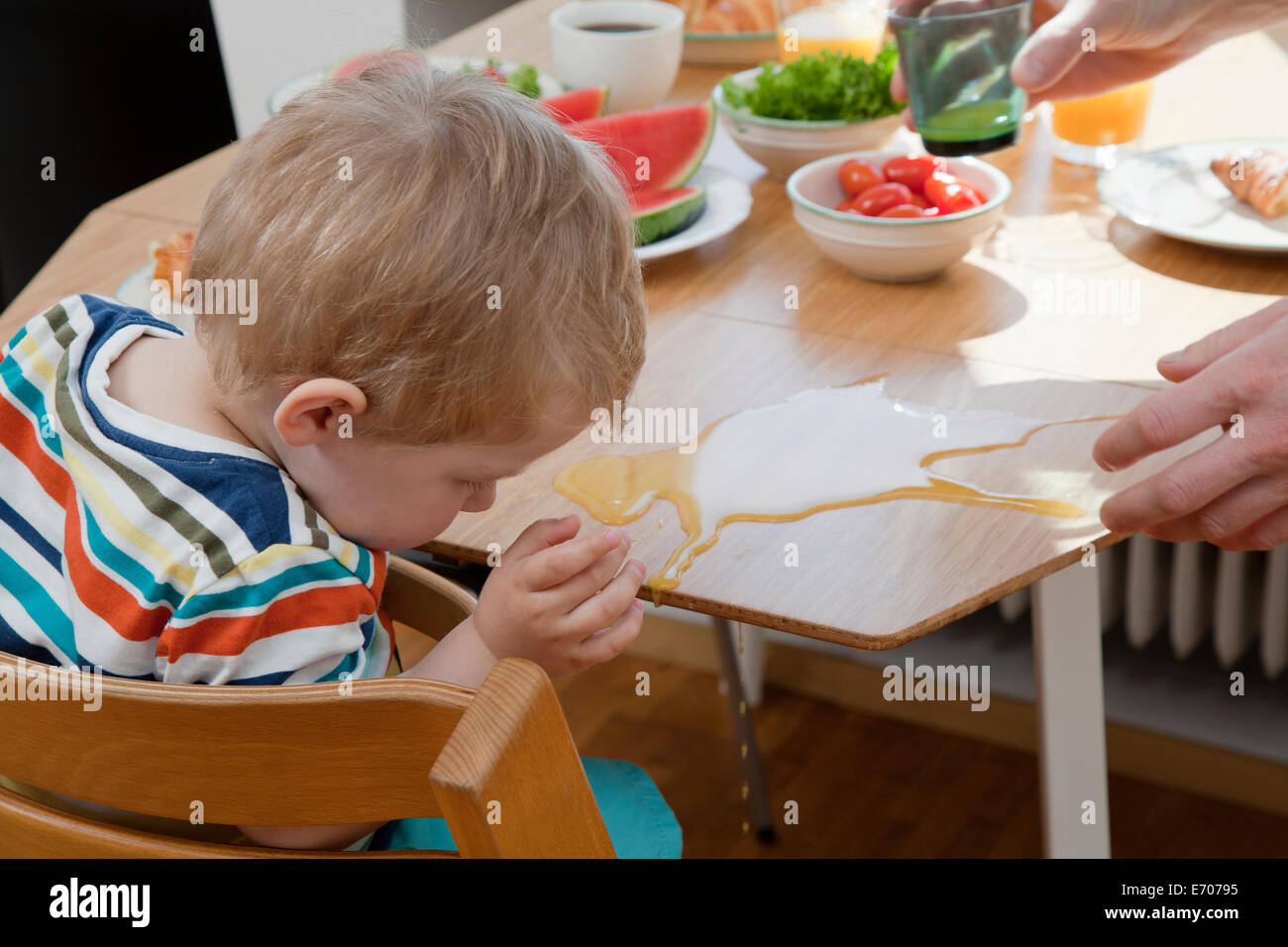 Male toddler accidentallyspilling orange juice at breakfast table Stock Photo