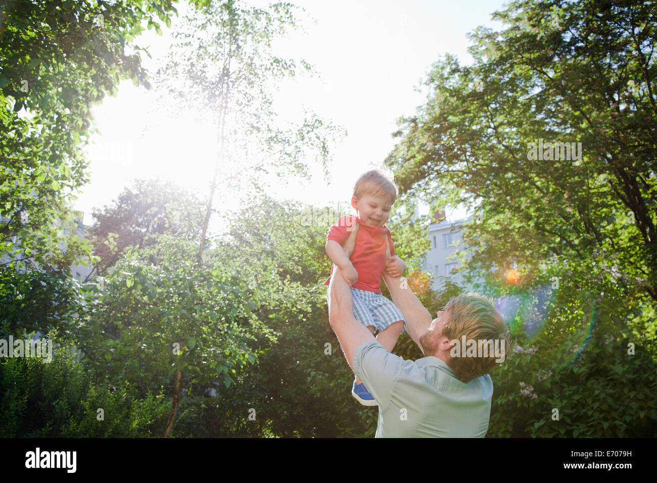 Father holding up toddler son in park Stock Photo