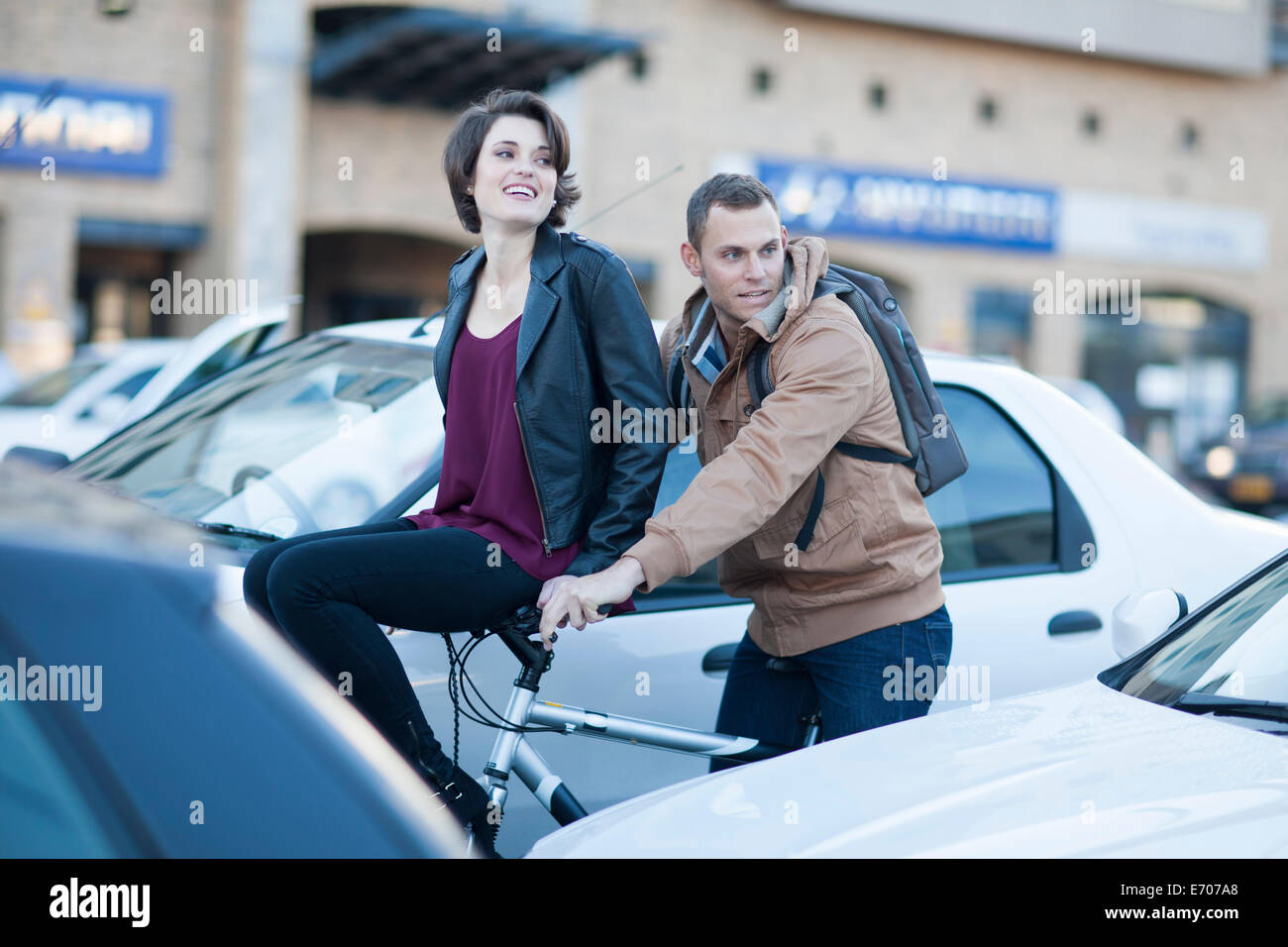 Young woman sitting on boyfriend's bicycle handlebar moving through