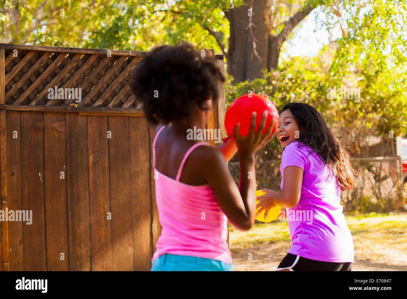 Girl chasing friend with water balloon in garden Stock Photo