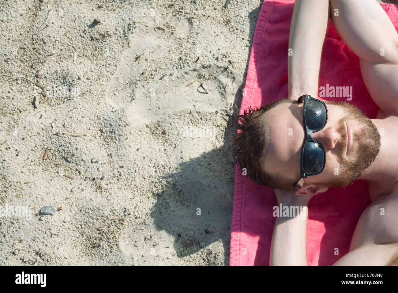 Overhead view of mid adult man in sunglasses sunbathing on sand Stock Photo