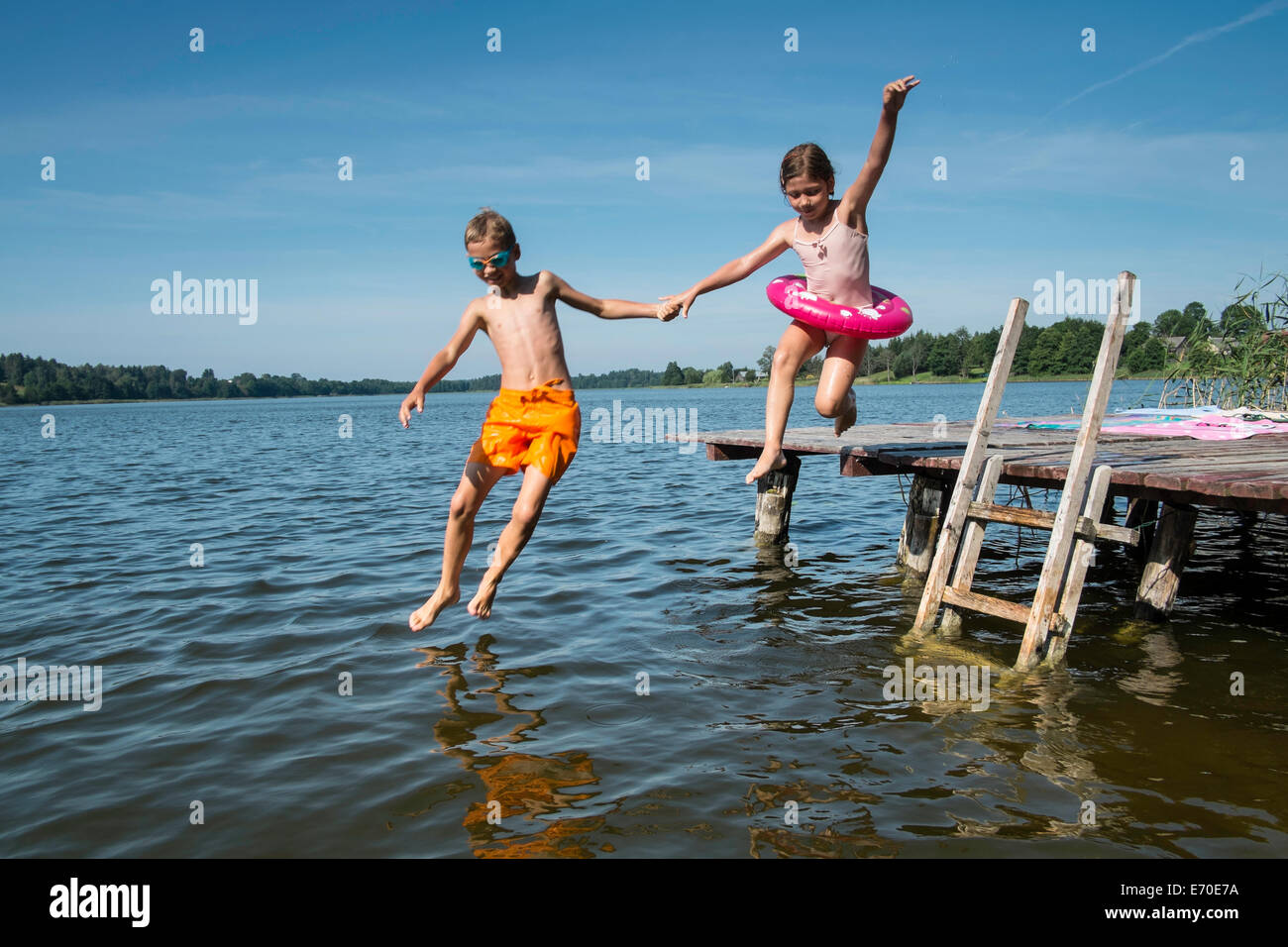 Brother and sister holding hands and jumping into lake Stock Photo