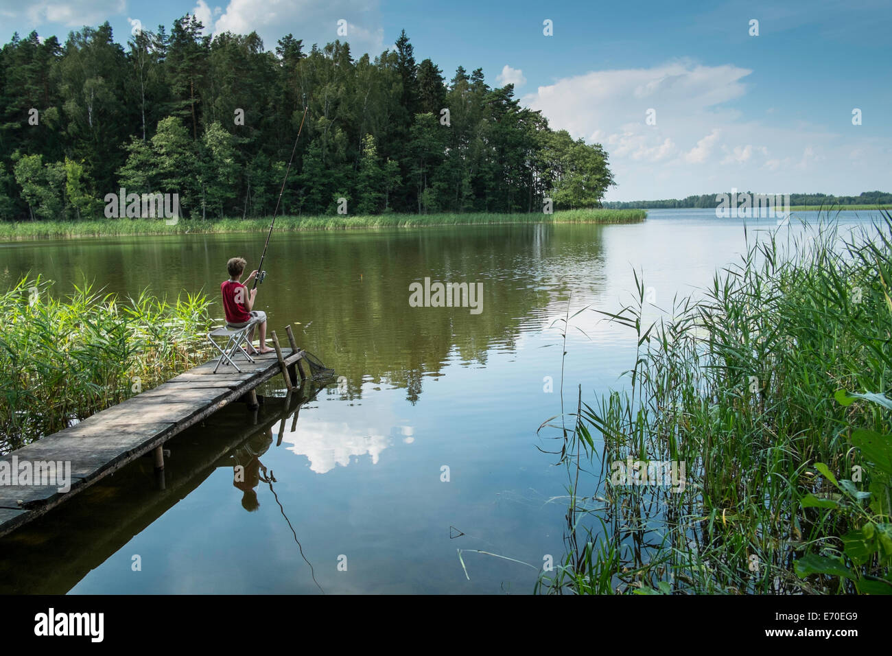 Boy fishing from a wooden pier, Giby, Poland Stock Photo