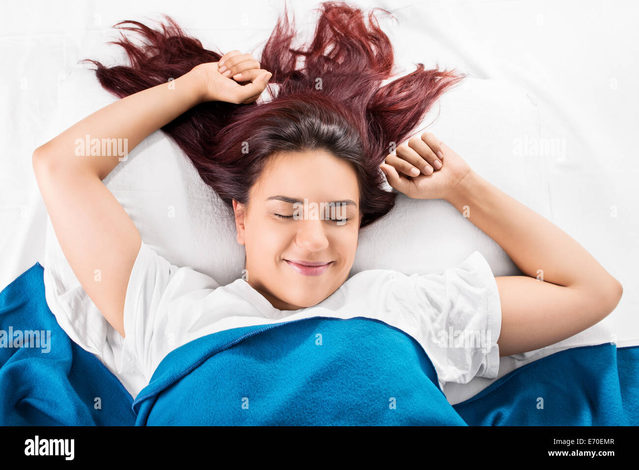 Close up of a beautiful smiling young girl waking up fresh and stretching in bed, isolated on white background. Stock Photo