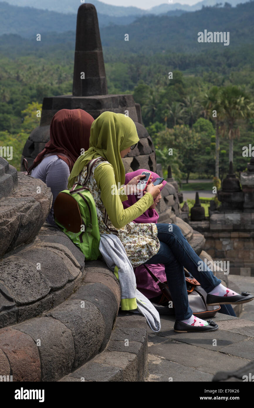 Borobudur, Java, Indonesia.  Young Indonesian Girl in Scarf and Levis Checking Cell Phones. Stock Photo