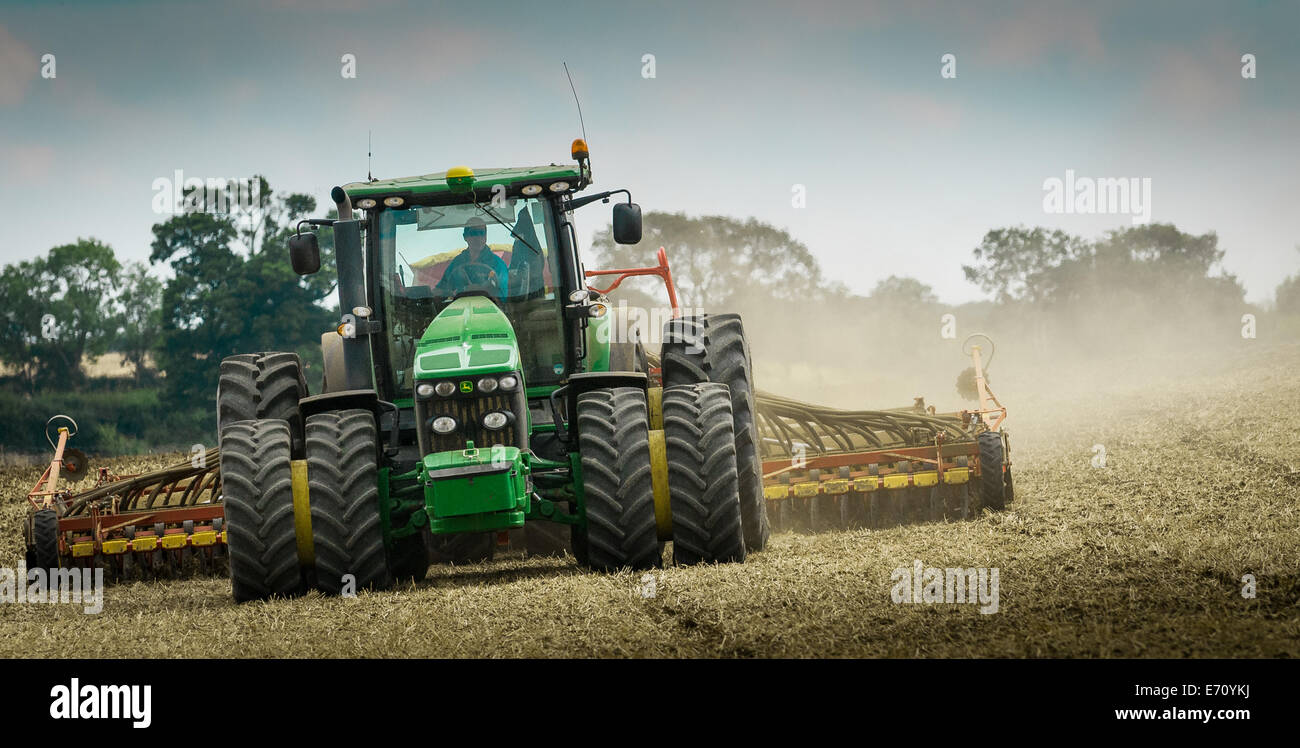 Farm tractor with a drill on the back, drilling, or sowing, grass seed onto a field that has been prepared or plowed (ploughed) Stock Photo