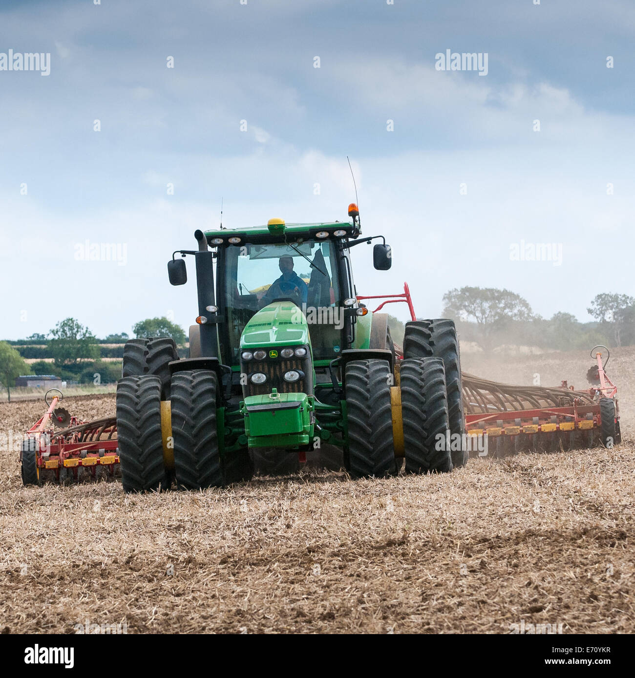 Farm tractor with a drill on the back, drilling, or sowing, grass seed onto a field that has been prepared or plowed (ploughed) Stock Photo