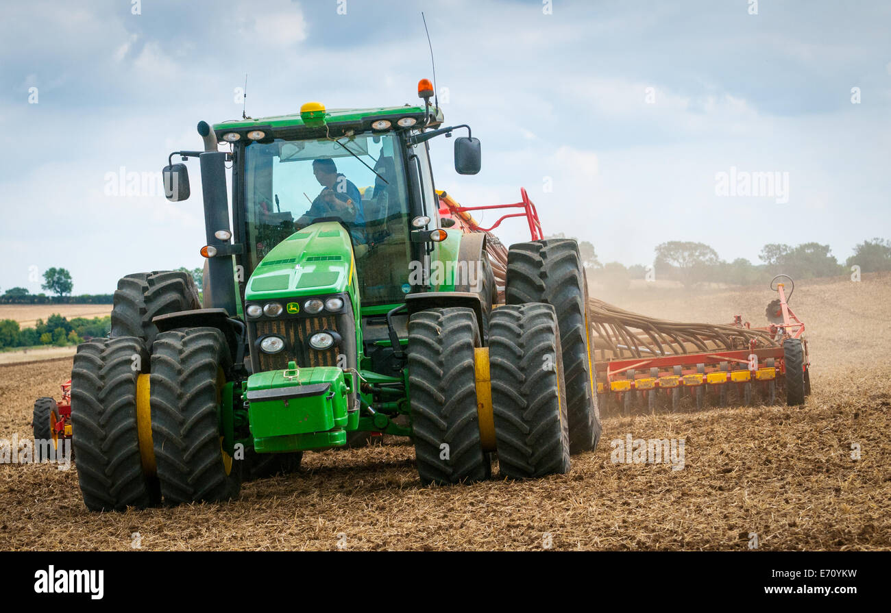 Farm tractor with a drill on the back, drilling, or sowing, grass seed onto a field that has been prepared or plowed (ploughed) Stock Photo