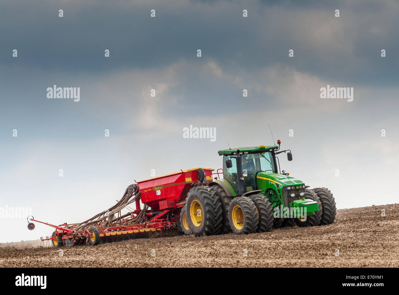 Farm tractor with a drill on the back, drilling, or sowing, grass seed onto a field that has been prepared or plowed (ploughed) Stock Photo