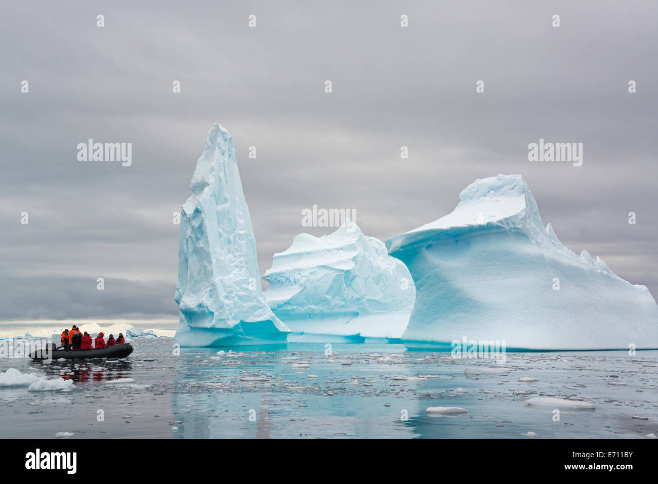 People in small inflatible zodiac rib boats passing towering sculpted icebergs around small islands of the Antarctic Peninsula. Stock Photo