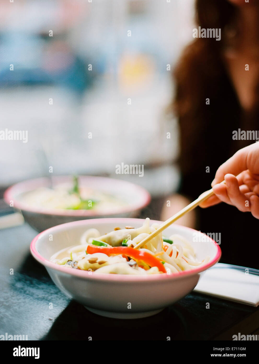 A person's hand holding chopsticks and stirring a dish of noodles. Stock Photo