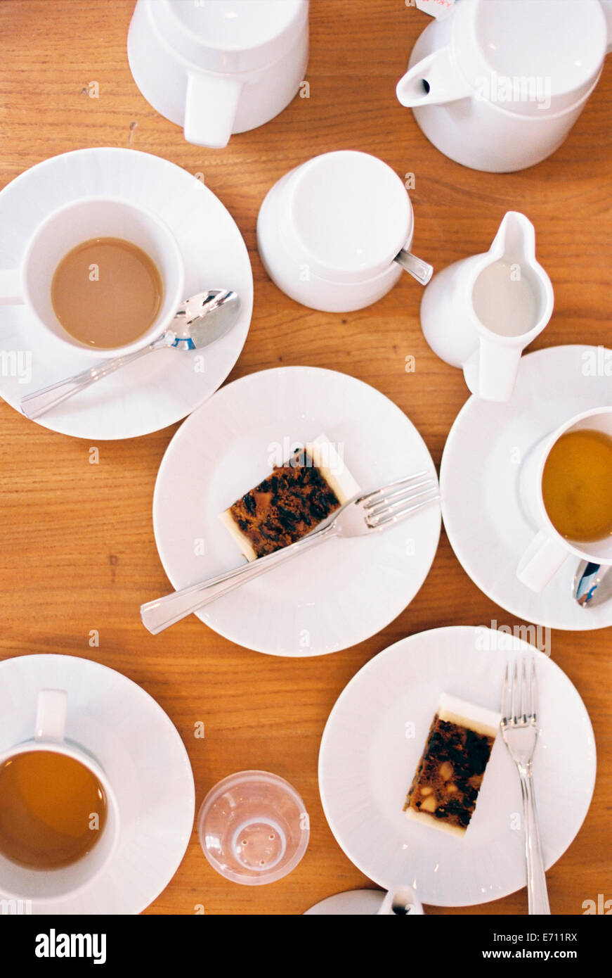 Overhead view of a table set with cups of tea, milk jugs and two slices of fruit cake on plates. Stock Photo