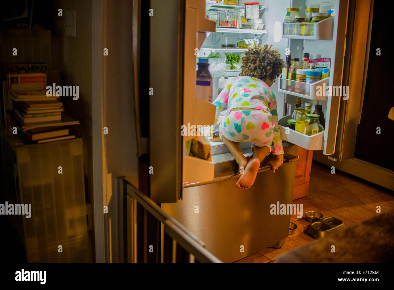 Rear view of girl sneaking food and drink from the refrigerator at night Stock Photo